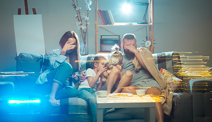 Image showing Happy family watching projector, TV, movies with popcorn in the evening at home. Mother, father and kids spending time together.