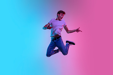 Image showing Young caucasian man\'s jumping high on gradient blue-pink studio background in neon light