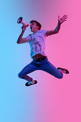 Image showing Young caucasian man\'s jumping high on gradient blue-pink studio background in neon light