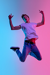 Image showing Young caucasian man\'s jumping high on gradient blue-pink studio background in neon light