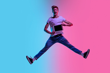 Image showing Young caucasian man\'s jumping high on gradient blue-pink studio background in neon light