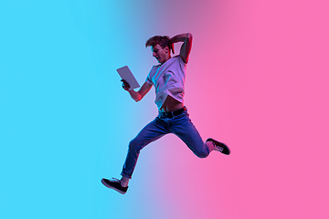 Image showing Young caucasian man\'s jumping high on gradient blue-pink studio background in neon light