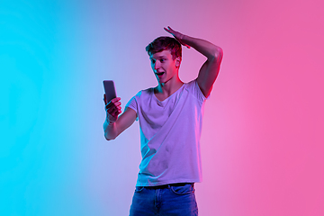 Image showing Young caucasian man\'s portrait on gradient blue-pink studio background in neon light