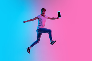 Image showing Young caucasian man\'s jumping high on gradient blue-pink studio background in neon light