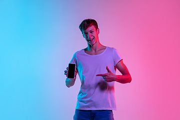 Image showing Young caucasian man\'s portrait on gradient blue-pink studio background in neon light