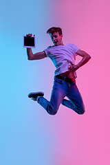Image showing Young caucasian man\'s jumping high on gradient blue-pink studio background in neon light