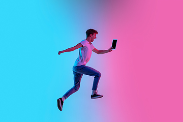 Image showing Young caucasian man\'s jumping high on gradient blue-pink studio background in neon light