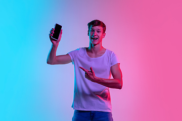 Image showing Young caucasian man\'s portrait on gradient blue-pink studio background in neon light