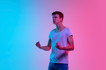 Image showing Young caucasian man\'s portrait on gradient blue-pink studio background in neon light