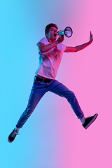 Image showing Young caucasian man\'s jumping high on gradient blue-pink studio background in neon light