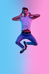 Image showing Young caucasian man\'s jumping high on gradient blue-pink studio background in neon light