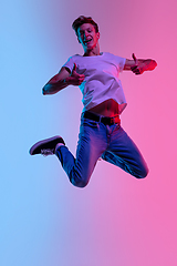 Image showing Young caucasian man\'s jumping high on gradient blue-pink studio background in neon light