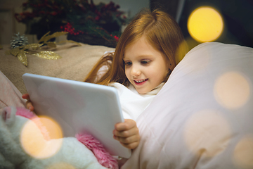 Image showing Happy caucasian little girl during video call or messaging with Santa using laptop and home devices, looks delighted and happy