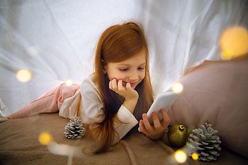 Image showing Happy caucasian little girl during video call or messaging with Santa using laptop and home devices, looks delighted and happy