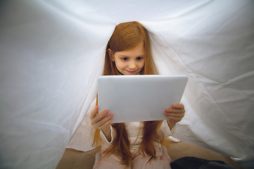 Image showing Happy caucasian little girl during video call or messaging with Santa using laptop and home devices, looks delighted and happy