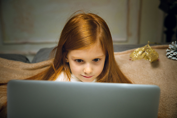 Image showing Happy caucasian little girl during video call or messaging with Santa using laptop and home devices, looks delighted and happy