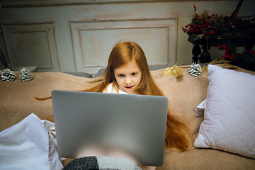 Image showing Happy caucasian little girl during video call or messaging with Santa using laptop and home devices, looks delighted and happy