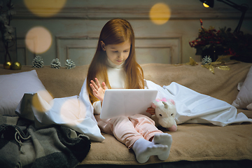 Image showing Happy caucasian little girl during video call or messaging with Santa using laptop and home devices, looks delighted and happy