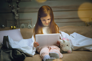 Image showing Happy caucasian little girl during video call or messaging with Santa using laptop and home devices, looks delighted and happy