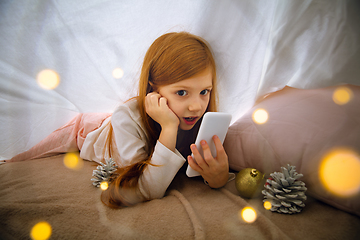 Image showing Happy caucasian little girl during video call or messaging with Santa using laptop and home devices, looks delighted and happy