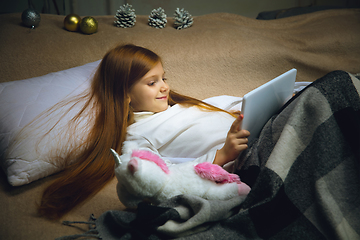 Image showing Happy caucasian little girl during video call or messaging with Santa using laptop and home devices, looks delighted and happy