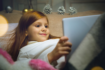 Image showing Happy caucasian little girl during video call or messaging with Santa using laptop and home devices, looks delighted and happy