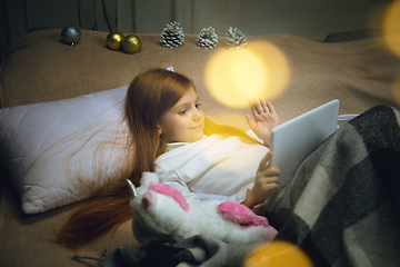 Image showing Happy caucasian little girl during video call or messaging with Santa using laptop and home devices, looks delighted and happy