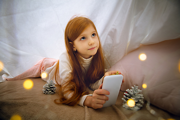 Image showing Happy caucasian little girl during video call or messaging with Santa using laptop and home devices, looks delighted and happy