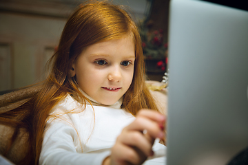 Image showing Happy caucasian little girl during video call or messaging with Santa using laptop and home devices, looks delighted and happy