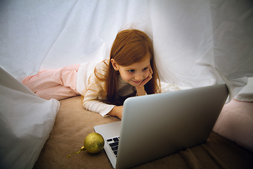 Image showing Happy caucasian little girl during video call or messaging with Santa using laptop and home devices, looks delighted and happy