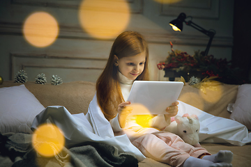 Image showing Happy caucasian little girl during video call or messaging with Santa using laptop and home devices, looks delighted and happy