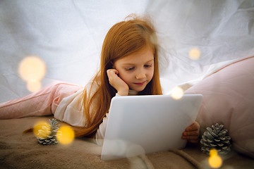 Image showing Happy caucasian little girl during video call or messaging with Santa using laptop and home devices, looks delighted and happy