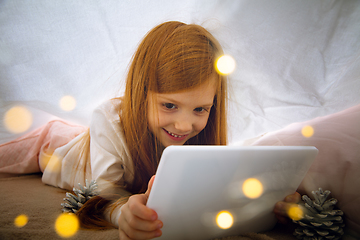 Image showing Happy caucasian little girl during video call or messaging with Santa using laptop and home devices, looks delighted and happy