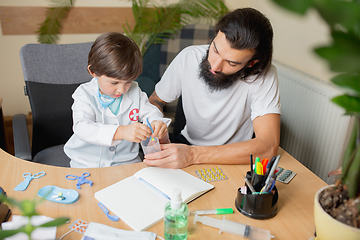 Image showing Little boy playing pretends like doctor examining a man in comfortabe medical office