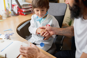 Image showing Little boy playing pretends like doctor examining a man in comfortabe medical office