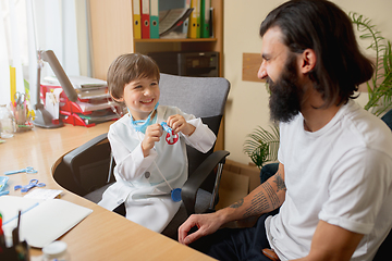 Image showing Little boy playing pretends like doctor examining a man in comfortabe medical office
