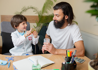 Image showing Little boy playing pretends like doctor examining a man in comfortabe medical office