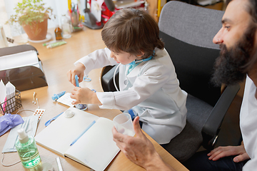 Image showing Little boy playing pretends like doctor examining a man in comfortabe medical office