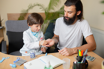 Image showing Little boy playing pretends like doctor examining a man in comfortabe medical office