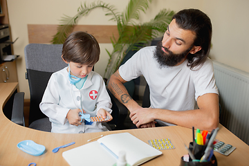 Image showing Little boy playing pretends like doctor examining a man in comfortabe medical office