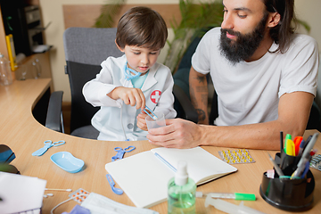 Image showing Little boy playing pretends like doctor examining a man in comfortabe medical office