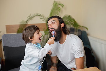 Image showing Little boy playing pretends like doctor examining a man in comfortabe medical office