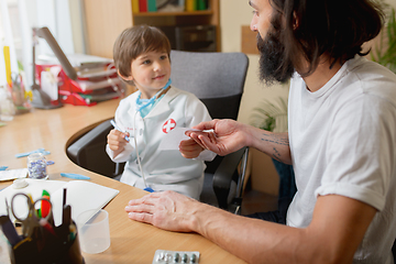 Image showing Little boy playing pretends like doctor examining a man in comfortabe medical office