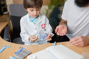 Image showing Little boy playing pretends like doctor examining a man in comfortabe medical office