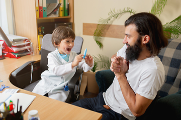 Image showing Little boy playing pretends like doctor examining a man in comfortabe medical office