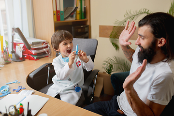 Image showing Little boy playing pretends like doctor examining a man in comfortabe medical office