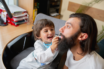 Image showing Little boy playing pretends like doctor examining a man in comfortabe medical office