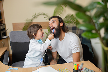 Image showing Little boy playing pretends like doctor examining a man in comfortabe medical office