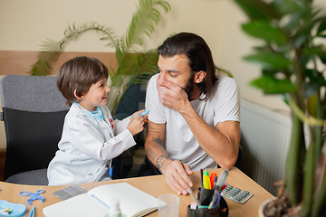 Image showing Little boy playing pretends like doctor examining a man in comfortabe medical office