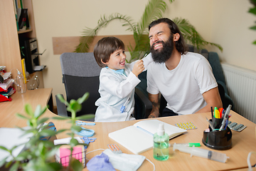 Image showing Little boy playing pretends like doctor examining a man in comfortabe medical office